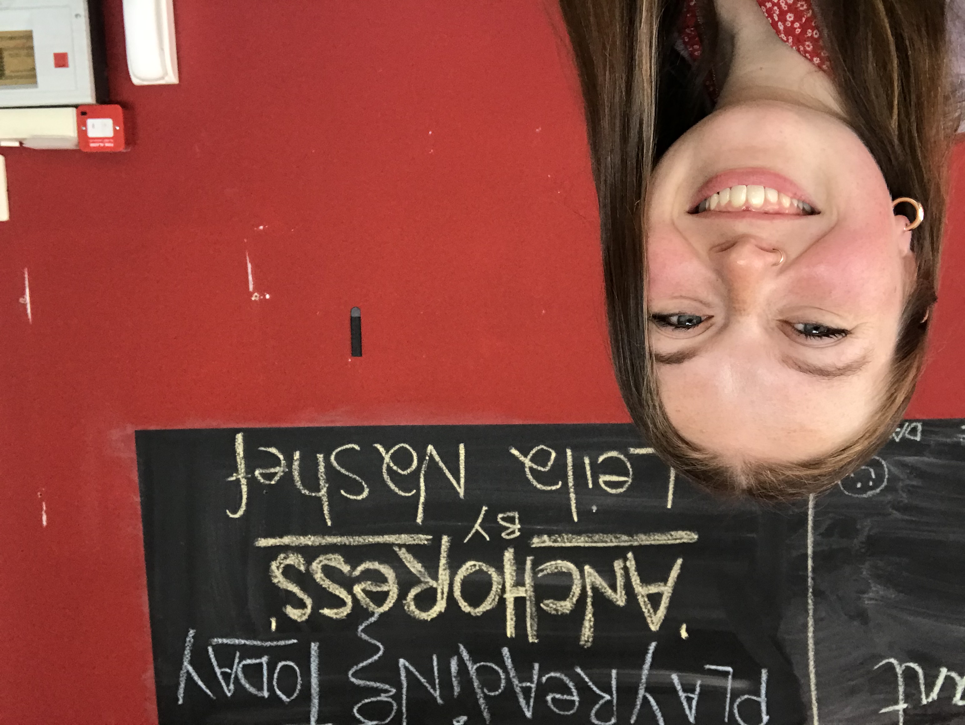 Dr Leila Nashef smiling in front of a sign for her play Anchoress